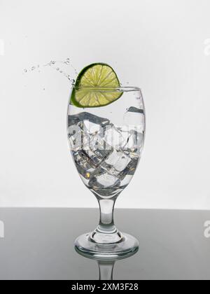 Ein Foto des Studiokonzepts, in dem eine Scheibe Kalk in ein Wasserglas fällt und ein Spritzer erzeugt. Stockfoto