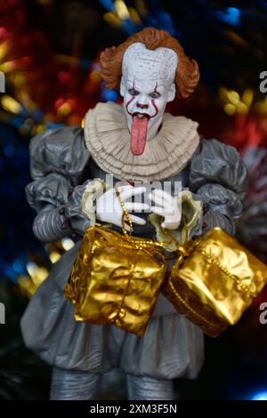 NECA Actionfigur von Pennywise Clown aus dem Horrorfilm IT. Spielzeug mit herunterhängender Zunge, Nahansicht. Kleine, helle Geschenkboxen, Weihnachtsbaum. Stockfoto