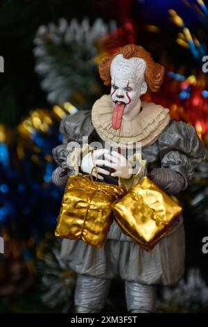 NECA Actionfigur von Pennywise Clown aus dem Horrorfilm IT. Spielzeug mit herunterhängender Zunge, Nahansicht. Kleine, helle Geschenkboxen, Weihnachtsbaum. Stockfoto