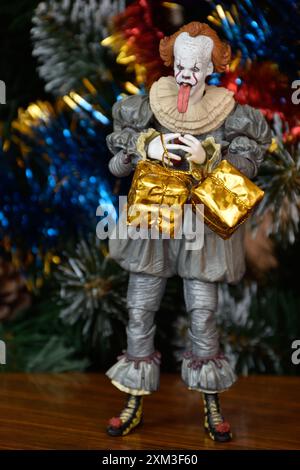 NECA Actionfigur von Pennywise Clown aus dem Horrorfilm IT. Spielzeug mit herunterhängender Zunge, Nahansicht. Kleine, helle Geschenkboxen, Weihnachtsbaum. Stockfoto