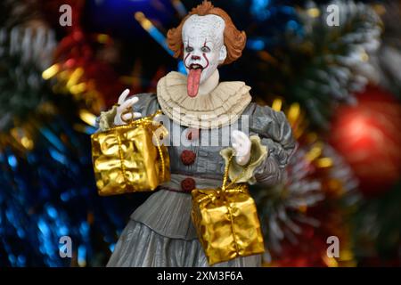 NECA Actionfigur von Pennywise Clown aus dem Horrorfilm IT. Spielzeug mit herunterhängender Zunge, Nahansicht. Kleine, helle Geschenkboxen, Weihnachtsbaum. Stockfoto