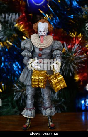 NECA Actionfigur von Pennywise Clown aus dem Horrorfilm IT. Spielzeug mit herunterhängender Zunge, Nahansicht. Kleine, helle Geschenkboxen, Weihnachtsbaum. Stockfoto