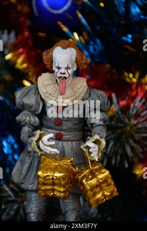 NECA Actionfigur von Pennywise Clown aus dem Horrorfilm IT. Spielzeug mit herunterhängender Zunge, Nahansicht. Kleine, helle Geschenkboxen, Weihnachtsbaum. Stockfoto