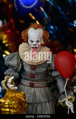 NECA Actionfigur von Pennywise Clown aus dem Horrorfilm IT. Gruseliges Spielzeug mit aufgehängter Zunge, Miniatur-Geschenkbox, roter Ballon. Weihnachtsbaum. Stockfoto