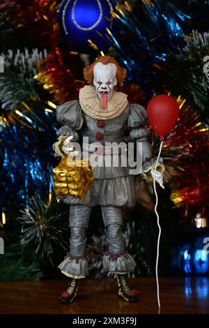 NECA Actionfigur von Pennywise Clown aus dem Horrorfilm IT. Gruseliges Spielzeug mit aufgehängter Zunge, Miniatur-Geschenkbox, roter Ballon. Weihnachtsbaum. Stockfoto