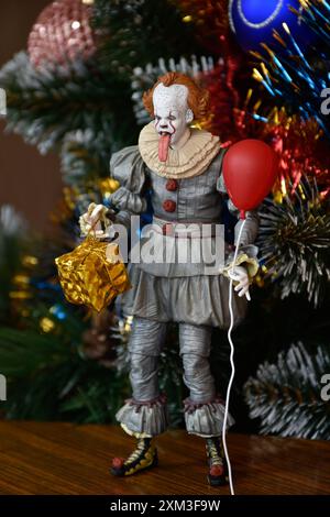 NECA Actionfigur von Pennywise Clown aus dem Horrorfilm IT. Gruseliges Spielzeug mit aufgehängter Zunge, Miniatur-Geschenkbox, roter Ballon. Weihnachtsbaum. Stockfoto