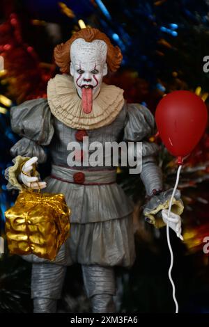 NECA Actionfigur von Pennywise Clown aus dem Horrorfilm IT. Gruseliges Spielzeug mit aufgehängter Zunge, Miniatur-Geschenkbox, roter Ballon. Weihnachtsbaum. Stockfoto