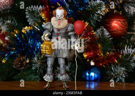 NECA Actionfigur von Pennywise Clown aus dem Horrorfilm IT. Gruseliges Spielzeug mit aufgehängter Zunge, Miniatur-Geschenkbox, roter Ballon. Weihnachtsbaum. Stockfoto