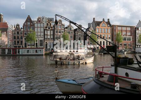 Ein Vergnügungsboot fährt entlang der Amstel vorbei an einer Reihe alter traditioneller Amsterdamer Häuser im Zentrum von Amsterdam. Stockfoto