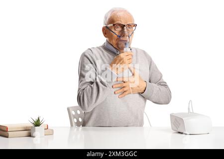 Älterer Mann mit Atemproblemen, der an einem Tisch sitzt und einen Vernebler auf weißem Hintergrund verwendet Stockfoto