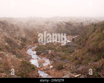 Eine felsige, karge Landschaft mit einem kleinen Bach, der durch sie fließt. Der Fluss ist von Felsen und Schmutz umgeben und der Himmel ist bedeckt. Die Szene hat einen Stockfoto