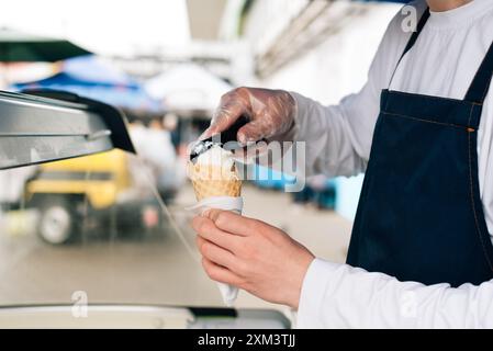 Waffelkegel mit köstlichem Erdbeereis in der Hand. Der Verkäufer gibt eine Eiskugel in eine Waffelkugel für Löffel Stockfoto