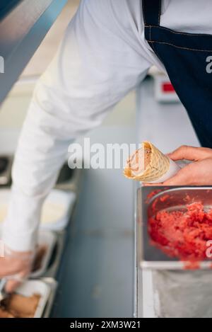 Waffelkegel mit köstlichem Erdbeereis in der Hand. Der Verkäufer gibt eine Eiskugel in eine Waffelkugel für Löffel Stockfoto