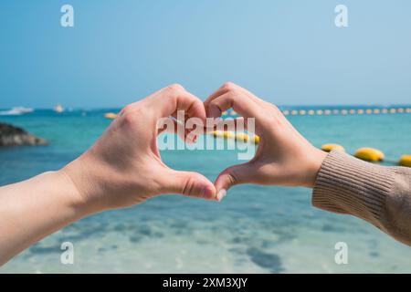 Zwei Hände bilden und eine Herzform am Strand machen. Das Konzept von Liebe und Zuneigung Stockfoto