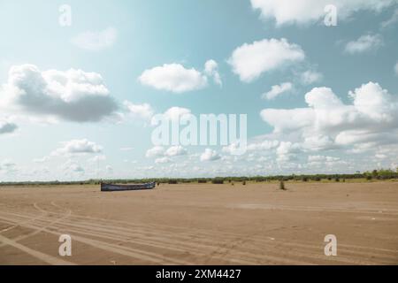 Altes hölzernes Fischerboot an einem Sandstrand verlassen, grüne Bäume in der Ferne, ein sonniger Tag im Sommer Stockfoto