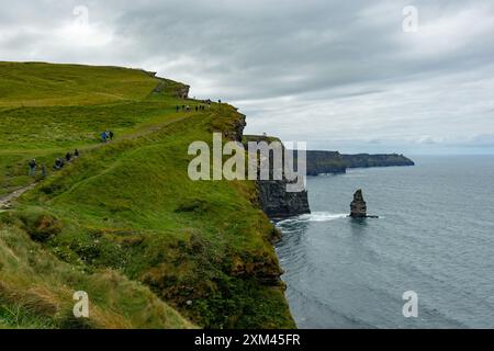 Touristen wandern an einem bewölkten Tag entlang der Cliffs of Moher in Irland mit Blick auf den Atlantischen Ozean Stockfoto