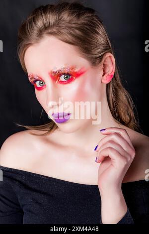 Modeporträt einer jungen kaukasischen Frau mit kräftigem rotem und lila Make-up, vor dunklem Hintergrund. Vertikales Foto. Nahaufnahme. Stockfoto