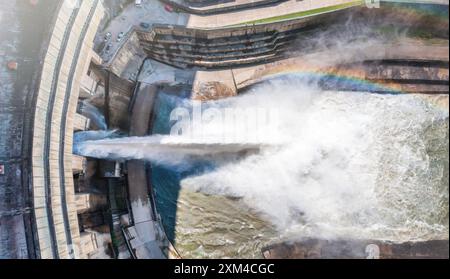 Aus der Vogelperspektive des Damms, der Wasser abgibt und einen starken Sprach- und Regenbogeneffekt erzeugt. Wasserkraft, erneuerbare Energien, Wasserwirtschaft und Ingenieurskunst. Stockfoto