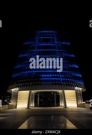 Ein beeindruckendes modernes Gebäude mit unverwechselbaren architektonischen Elementen, die bei Nacht mit blauem Licht beleuchtet werden und zeitgenössisches Design und städtische Landschaft bieten. Stockfoto