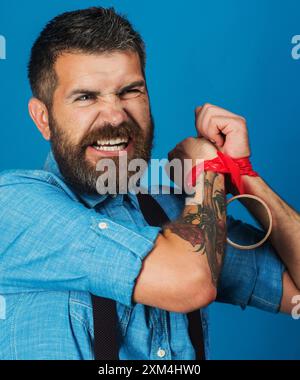 Wütender Mann im Jeanshemd, der Scotch Tape an den Händen reißt. Entführung, Verbrechen, Gewalt und Geiselnahme. Wütender bärtiger Mann mit rotem Klebeband Stockfoto