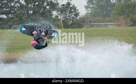 Kent, vereinigtes Königreich, 22. August 2023 Ein männlicher Wakeboarder-Athlet in einem Schutzhelm und einer Weste reitet auf einem Wasserbrett in einer Sommerbucht Stockfoto
