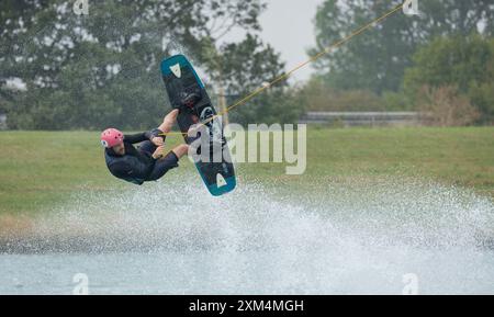 Kent, vereinigtes Königreich, 22. August 2023 Ein männlicher Wakeboarder-Athlet in einem Schutzhelm und einer Weste reitet auf einem Wasserbrett in einer Sommerbucht Stockfoto