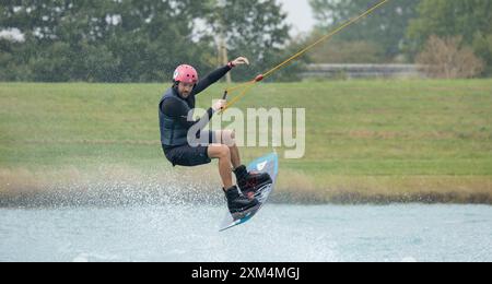Kent, vereinigtes Königreich, 22. August 2023 Ein männlicher Wakeboarder-Athlet in einem Schutzhelm und einer Weste reitet auf einem Wasserbrett in einer Sommerbucht Stockfoto