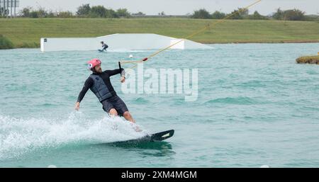 Kent, vereinigtes Königreich, 22. August 2023 Ein männlicher Wakeboarder-Athlet in einem Schutzhelm und einer Weste reitet auf einem Wasserbrett in einer Sommerbucht Stockfoto