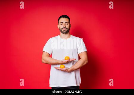 Schöner großer bärtiger weißer Mann mit dunklen Haaren mit Mandarine auf rotem Hintergrund Stockfoto