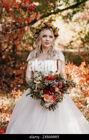 Blondes Mädchen in einem Hochzeitskleid im Herbstwald vor wilden roten Trauben Stockfoto