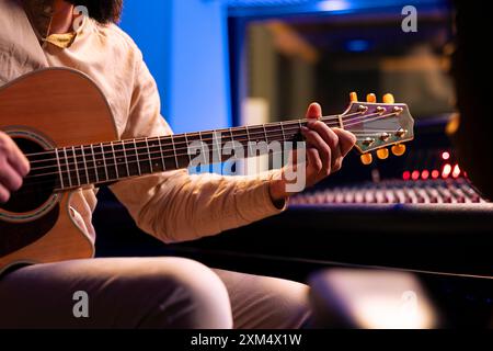 Talentierter Sänger, der elektroakustische Gitarre im Musikstudio spielt und einen neuen Hit mit einem Toningenieur im Kontrollraum komponiert. Künstler, der Titel mit Instrument und Stereo-Ausrüstung erstellt. Stockfoto