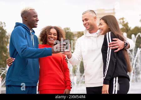 Multiethnische Freunde in Sportbekleidung, die Kaffeetassen toasten. Afroamerikanischer asiatischer Kaukasier, der Zeit zusammen verbringt. Multirassische Freundschaft. Glückliche lächelnde Paare im Park. Stockfoto