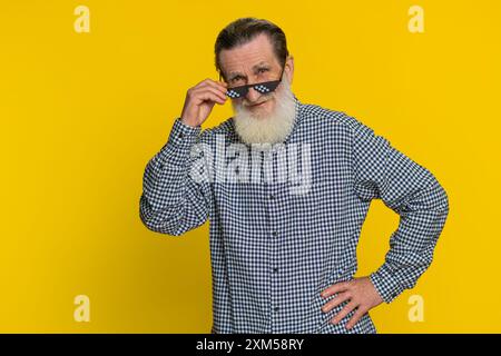 Porträt eines aufgeregten, stilvollen älteren Mannes mit schwarzer Sonnenbrille, charmantem Lächeln, erfolgreichem Sieg, guten positiven Nachrichten. Glücklicher älterer Großvater Rentner auf gelbem Hintergrund Stockfoto