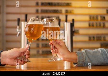 Nahaufnahme von zwei Händen, die in einer modernen Bar ein Glas Craft-Bier anstoßen. Die Atmosphäre ist warm und einladend, perfekt für ein geselliges Treffen oder tagsüber Stockfoto