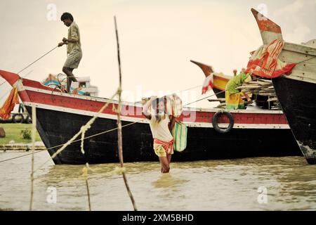 Ein Mann trägt sein Gepäck, während er auf flachem Wasser zwischen Booten läuft, die am Haldi-Fluss in Haldia, Purba Medinipur, Westbengalen, Indien ankerten. Laut einem von den Vereinten Nationen am 28. Februar 2022 veröffentlichten Bericht des Zwischenstaatlichen Ausschusses für Klimaänderungen werden in den nächsten 30 Jahren erstaunliche 143 Millionen Menschen durch steigende Meere, Dürre, sengende Temperaturen und andere Klimakatastrophen entwurzelt. Stockfoto