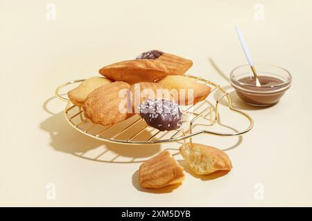 Raster mit köstlichen Madeleinen und Schüssel Schokoladenpaste auf beigem Hintergrund Stockfoto