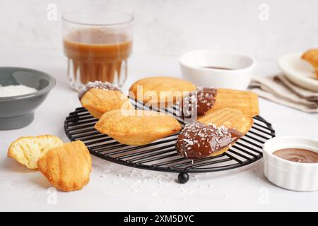 Gitter mit köstlichen Madeleinen und Schüssel Schokoladencreme auf weißem Hintergrund Stockfoto