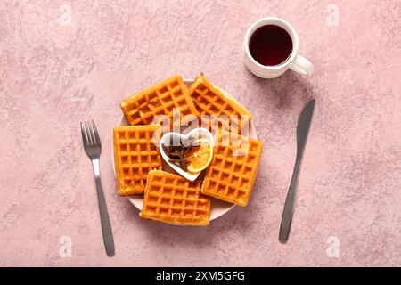 Teller mit leckeren belgischen Waffeln und einer Tasse Kaffee auf rosafarbenem Hintergrund Stockfoto