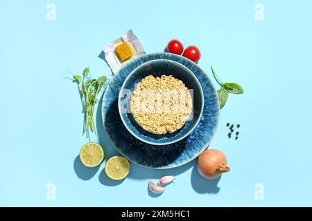 Schüssel mit rohen Instantnudeln und verschiedenen Zutaten auf blauem Hintergrund Stockfoto