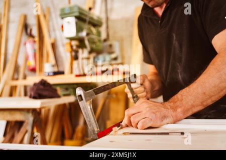 Zimmermann schneidet in einer Werkstatt, umgeben von Werkzeugen und Materialien, vorsichtig mit einer Bügelsäge ein Stück Holz. Er arbeitet mit Präzision und Konzentration Stockfoto