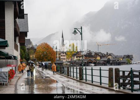 Hallstatt, Österreich - 31. Oktober 2023 : Regentag in Hallstatt, Österreich. Die Leute laufen entlang einer kopfsteingepflasterten Straße mit Blick auf den See und die Berge. Stockfoto