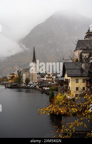 Hallstatt, Österreich - 31. Oktober 2023 : Ein Kirchturm durchsticht die Wolken über dem malerischen Dorf Hallstatt. Der See reflektiert das Grau Stockfoto