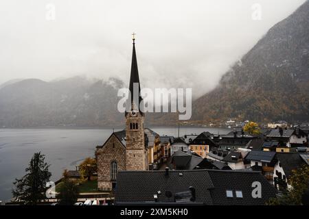 Hallstatt, Österreich - 31. Oktober 2023 : Ein Kirchturm durchdringt die Wolken oberhalb von Hallstatt. Die Stadt liegt eingebettet unter einem Berg, Surro Stockfoto