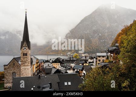 Hallstatt, Österreich - 31. Oktober 2023 : Ein malerisches Dorf in den österreichischen Alpen, mit einem hohen Kirchturm und Nebel, der über den Moun rollt Stockfoto