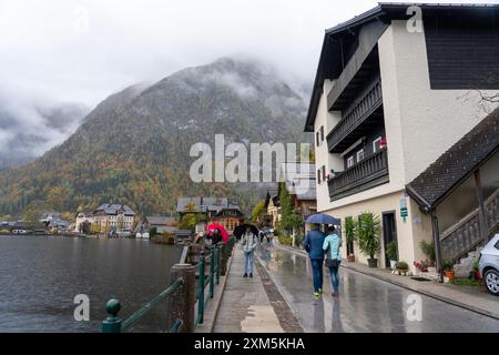 Hallstatt, Österreich - 31. Oktober 2023 : Regentag in Hallstatt, Österreich, mit Blick auf See und Berge. Die Leute laufen die Straße entlang mit Umbr Stockfoto