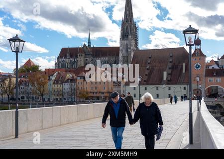 Regensburg, Deutschland - 06. November 2023 : ein älteres Ehepaar geht Hand in Hand auf einem Steinweg in Regensburg, mit Dom und Uhrenschleppe Stockfoto
