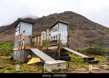 Im Sommer befinden sich auf dem Grizzly Lake Backcountry Campingplatz im Norden Kanadas Toiletten und Berggipfel im Hintergrund. Stockfoto