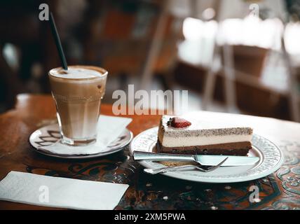 Alanya, Türkei, 17. September 2020: Erdbeer-Schokoladenkuchen mit Cappuccino auf einem Holztisch in einem Café Stockfoto