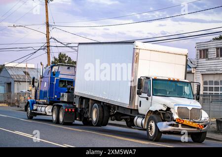 Mobile blaue Pannenhilfe leistungsstarker Abschleppwagen Sattelzugmaschine Abschleppen gebrochen nach Unfall Tag Kabine Sattelzugwagen mit Kastenanhänger fährt auf der Straße Stockfoto