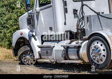 Weißer, großer Lkw für industrielle Anwendungen mit einem verdrehten Rad und einem durchbrochenen Reifen, der auf der Straßenschulter außer Betrieb steht und auf mobile Fahrzeuge wartet Stockfoto